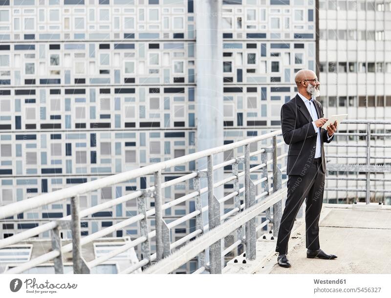 Geschäftsmann steht auf Bürogebäude mit digitalem Tablet Smartphone iPhone Smartphones stehen stehend unterwegs auf Achse in Bewegung Businessmann