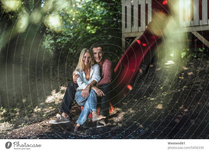Glückliches Paar sitzt auf der Rutsche eines Gartenhäuschens im Wald sitzen sitzend lächeln Forst Wälder glücklich glücklich sein glücklichsein Pärchen Paare
