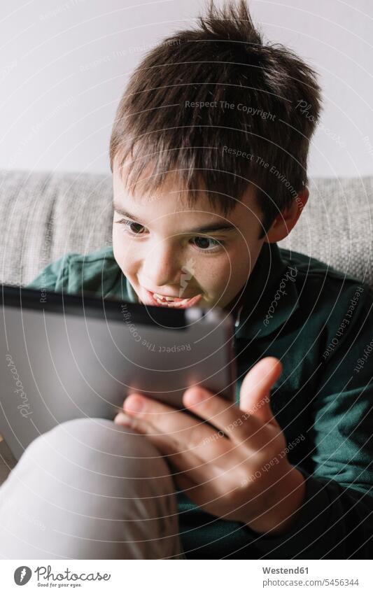 Porträt eines lachenden Jungen, der auf der Couch im Wohnzimmer sitzt und ein Tablett benutzt benutzen benützen Tablet Computer Tablet-PC Tablet PC iPad