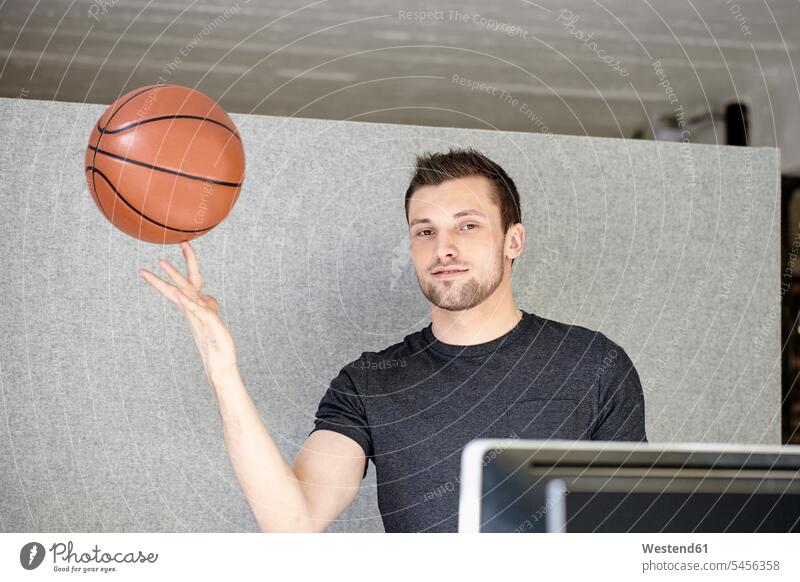 Junger Mann arbeitet im Büro und balanciert einen Basketball lächeln junger Mann junge Männer Ball Bälle sitzen sitzend sitzt balancieren Balance Office Büros