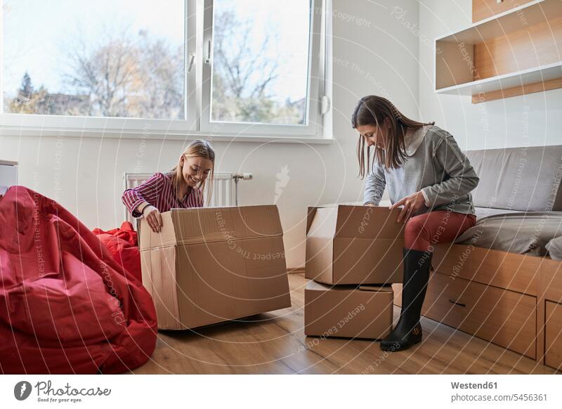 Zwei junge Frauen packen in einem Raum Pappkartons aus Freundinnen auspacken Zimmer Räume Karton Kartons weiblich Freunde Freundschaft Kameradschaft Erwachsener