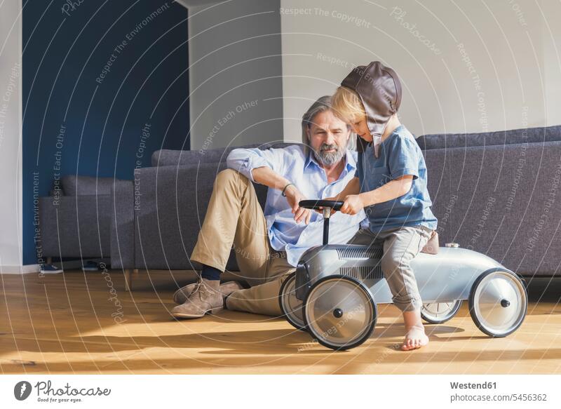 Großvater spielt mit Enkel, sitzt auf Spielzeugauto Opa Großpapa Großpapas Opas Opi Großväter Opis Enkelsöhne Enkelsohn Auto Autos Spielzeugautos Wohnzimmer
