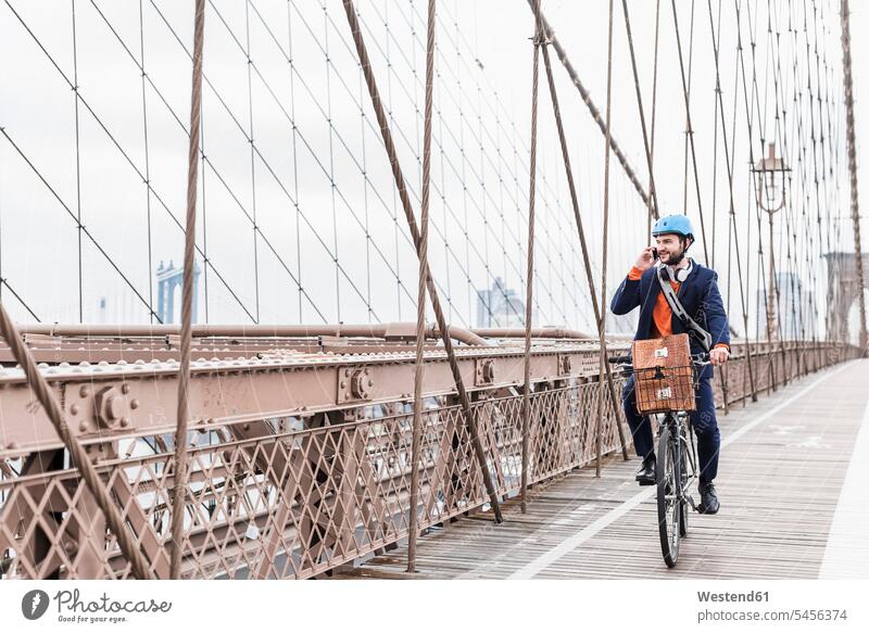 USA, New York City, Mann auf dem Fahrrad auf der Brooklyn Bridge mit Mobiltelefon New York State Handy Handies Handys Mobiltelefone Männer männlich telefonieren