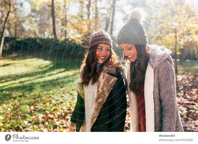 Zwei hübsche Frauen gehen in einem herbstlichen Wald spazieren Freundinnen lächeln weiblich Forst Wälder Herbst schön gehend geht Freunde Freundschaft