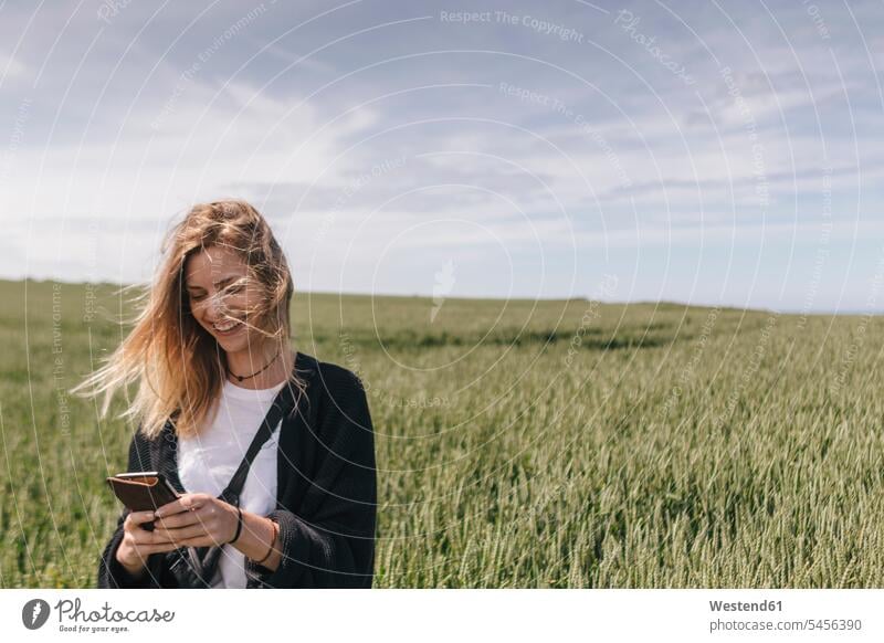 Junge Frau mit Smartphone, im Feld stehend iPhone Smartphones lächeln simsen Handy Mobiltelefon Handies Handys Mobiltelefone checken gute Nachrichten