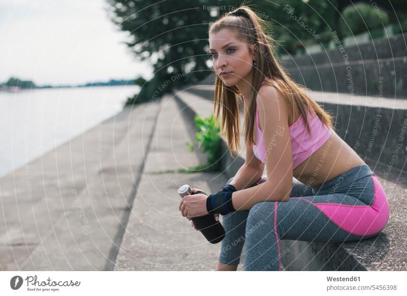 Sportliche Frau macht eine Pause am Flussufer trainieren sportlich weiblich Frauen sitzen sitzend sitzt Erwachsener erwachsen Mensch Menschen Leute People