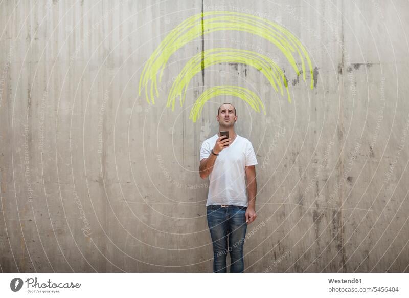 Mann hält Handy mit gelbem Kreide-Wifi-Zeichen über seinem Kopf Symbol Symbole symbolisch Darstellung darstellen Mobiltelefon Handies Handys Mobiltelefone Wand