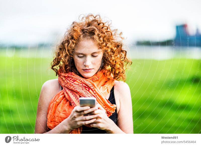 Porträt einer jungen Frau mit lockigem roten Haar beim Blick auf ein Mobiltelefon weiblich Frauen Portrait Porträts Portraits Erwachsener erwachsen Mensch