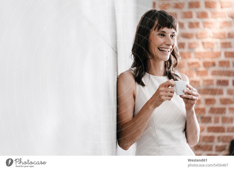Frau trinkt Kaffee im Büro, lehnt an Wand stehen stehend steht weiblich Frauen trinken Getränk Getraenk Getränke Getraenke Food and Drink Lebensmittel