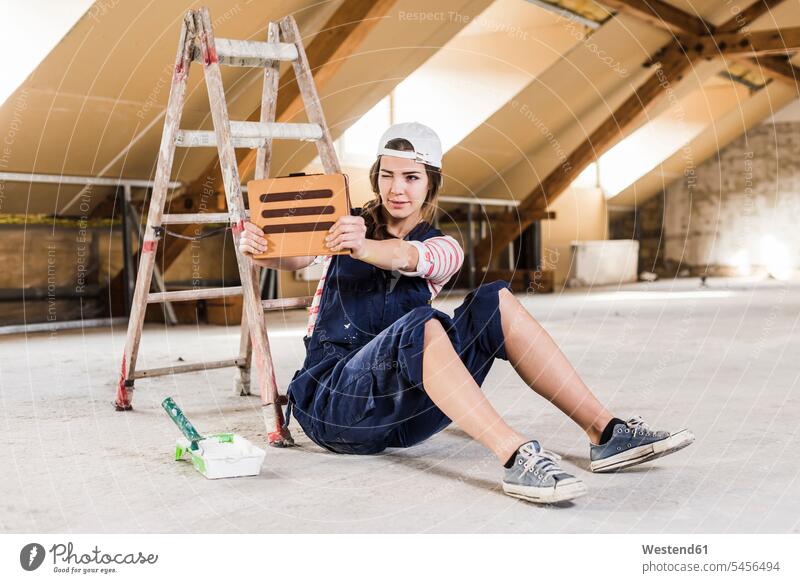 Junge Frau sitzt auf einer Baustelle und benutzt ein digitales Tablett renovieren Renovierung junge Frau junge Frauen Leiter Leitern Heimwerken Do-it-Yourself