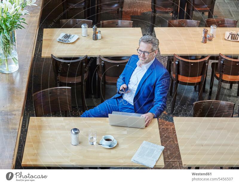 Reifer Geschäftsmann im Café mit Laptop, Handy und Ohrstöpseln Notebook Laptops Notebooks Cafe Kaffeehaus Bistro Cafes Cafés Kaffeehäuser Businessmann