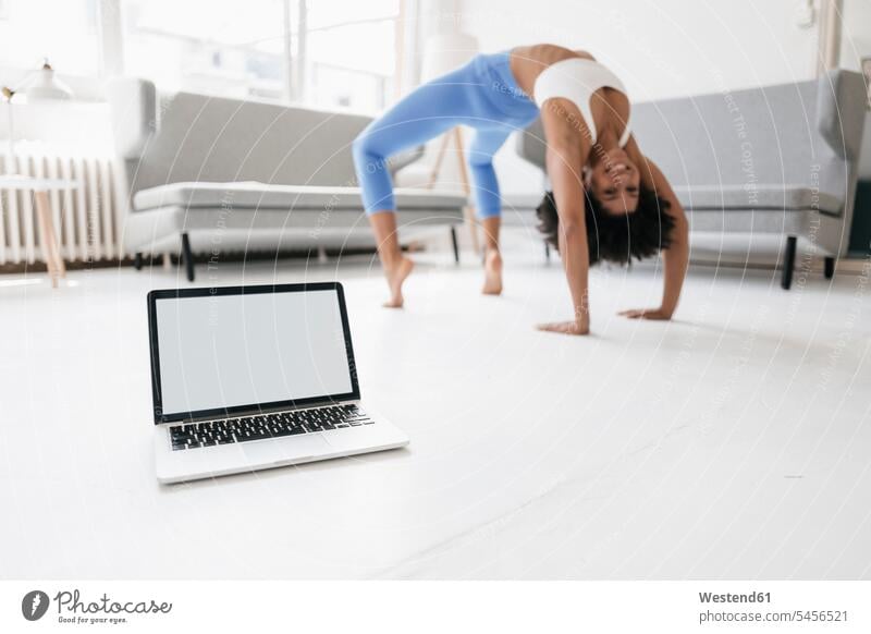 Junge Frau praktiziert Yoga mit Laptop an ihrer Seite Online fit Notebook Laptops Notebooks lernen üben ausüben Übung trainieren weiblich Frauen Training