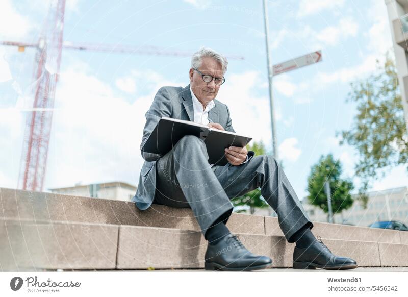 Porträt eines älteren Geschäftsmannes auf einer Treppe sitzend mit Notebook vor einem Baukran Businessmann Businessmänner Geschäftsmänner Geschäftsleute