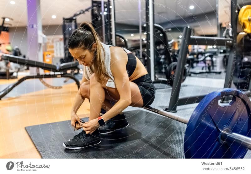 Junge Frau bindet ihre Schuhe im Fitnessstudio Fitnessclubs Fitnessstudios Turnhalle Hantel Hanteln trainieren weiblich Frauen fit Gesundheit gesund Sport