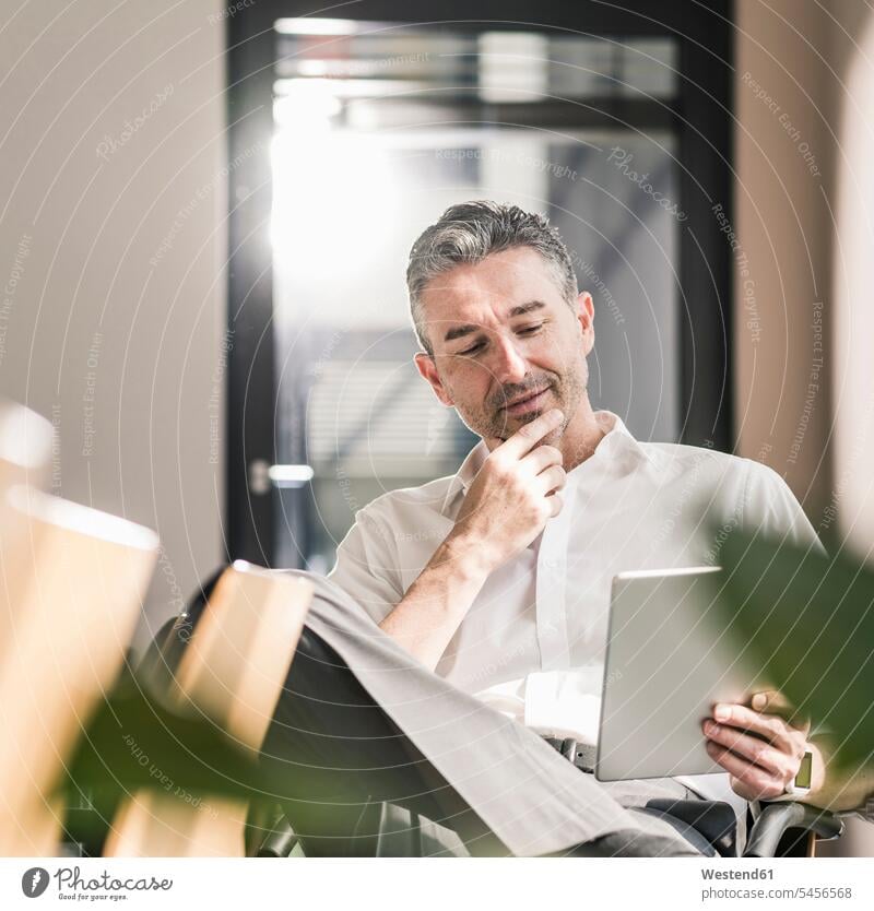 Lächelnder Geschäftsmann sitzt in einem Büro und benutzt ein Tablett Portrait Porträts Portraits Tablet Computer Tablet-PC Tablet PC iPad Tablet-Computer