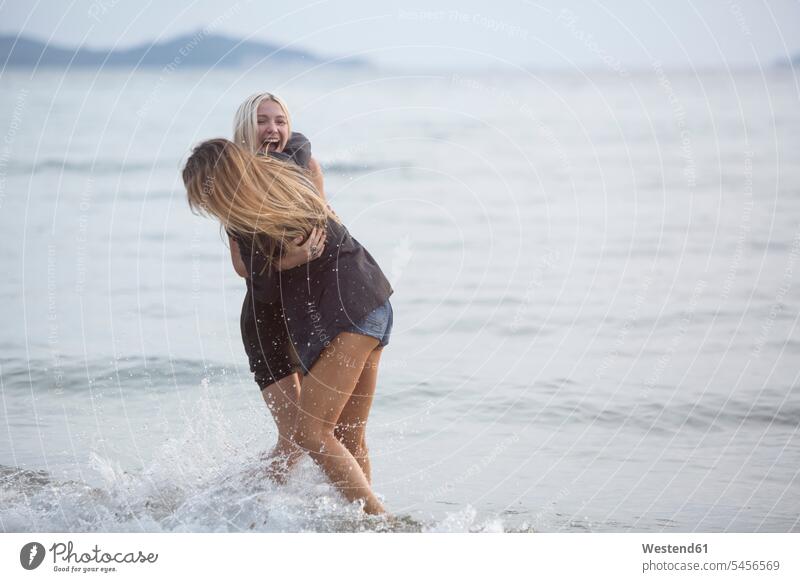Zwei junge Frauen amüsieren sich im Meer Spaß Spass Späße spassig Spässe spaßig Freundinnen Meere Paar Pärchen Paare Partnerschaft lachen glücklich Glück