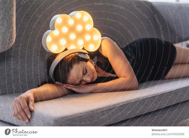 Auf Couch liegende Frau mit Kopfhörern und beleuchteter Wolke über ihr liegt Kopfhoerer entspannt entspanntheit relaxt weiblich Frauen Entspannung relaxen