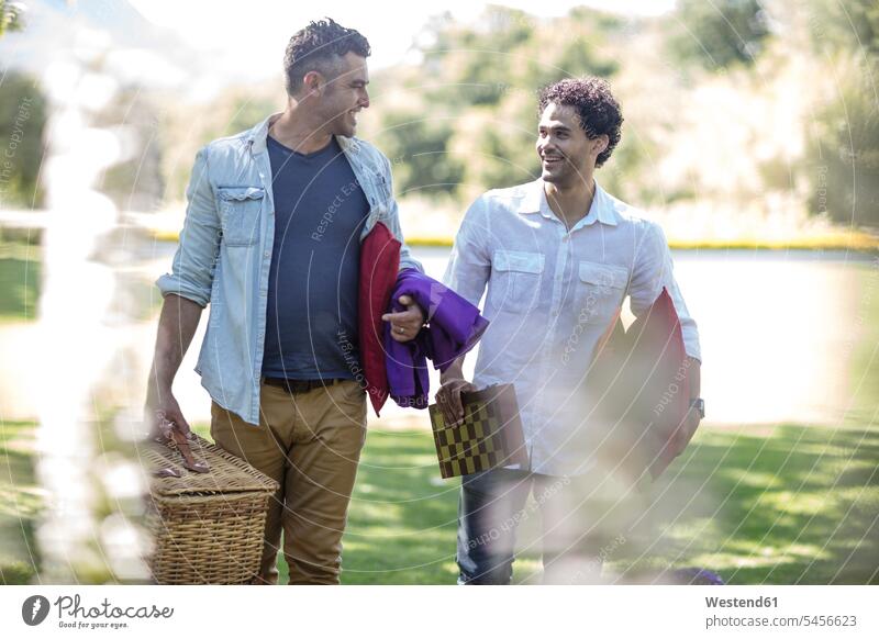 Zwei Freunde spazieren im Park mit Picknickkorb und Schachbrett lächeln Mann Männer männlich Freundschaft Kameradschaft Erwachsener erwachsen Mensch Menschen