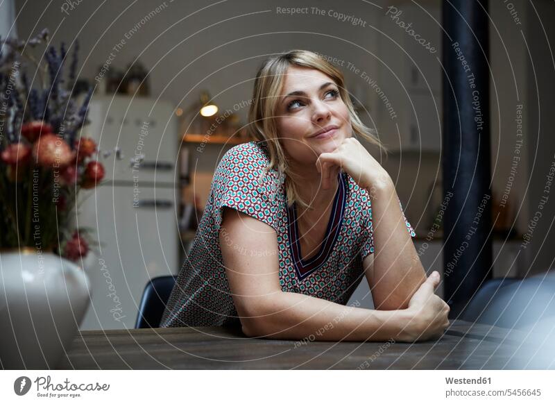 Porträt einer lächelnden Frau, die am Tisch in der Küche sitzt und nachdenkt Küchen weiblich Frauen Portrait Porträts Portraits sitzen sitzend nachdenken