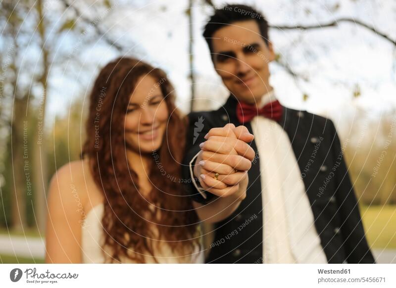 Glückliches Brautpaar steht im Park, hält Hände, zeigt Ehering Hände halten Haendchen halten Hand halten Haende halten Händchen halten Hand in Hand Paar Pärchen