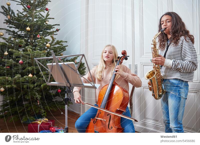 Zwei Mädchen spielen Cello und Saxophon am Weihnachtsbaum weiblich Musik Christbaum Weihnachtsbäume Weihnachtsbaeume Christbäume Christbaeume Kind Kinder Kids