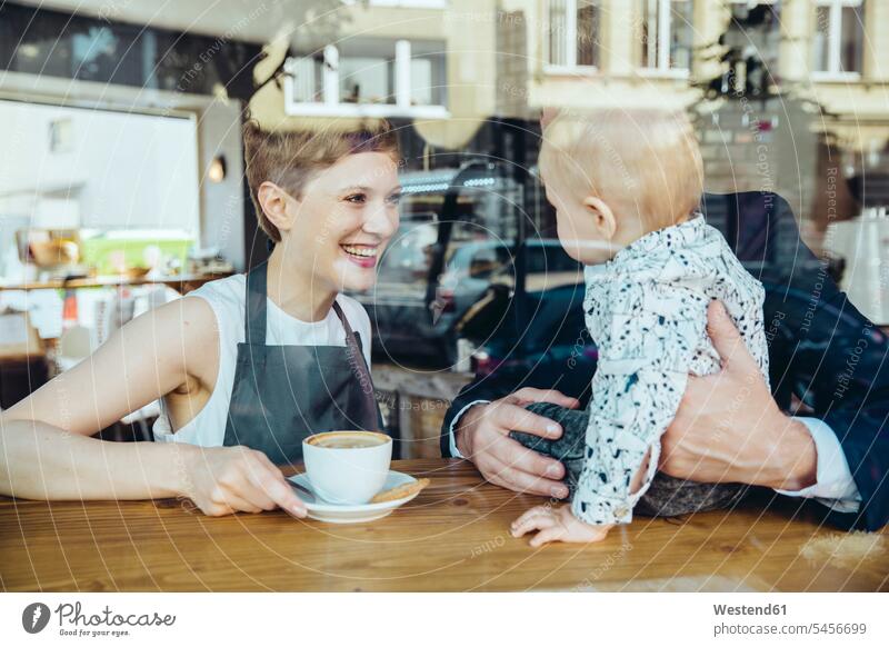 Kellnerin serviert lächelnden Kunden mit Baby im Cafe Kaffee Kaffeehaus Bistro Cafes Café Cafés Kaffeehäuser Portrait Porträts Portraits Restaurantfachfrau