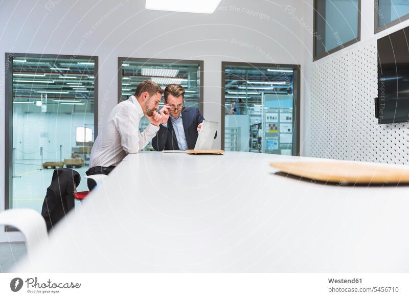 Zwei Geschäftsleute sitzen in einem modernen Büro und diskutieren vor einem Laptop Kollegen Arbeitskollegen Team Geschäftsmann Businessmann Businessmänner