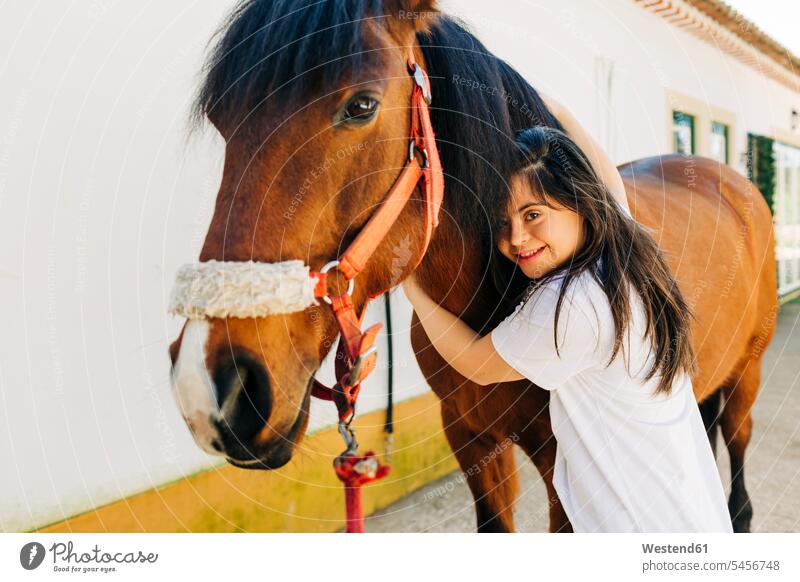 Teenager mit Down-Syndrom kümmert sich um Pferd und bereitet Pferd zum Reiten vor knuddeln schmusen Arm umlegen Umarmung Umarmungen freuen Glück glücklich sein