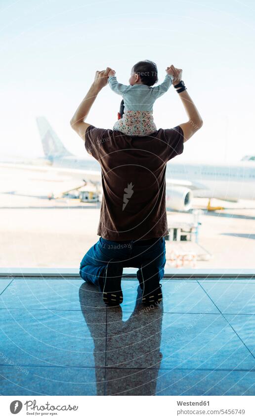 Mann trägt ein kleines Mädchen auf den Schultern auf dem Flughafen und schaut auf die Flugzeuge, Rückansicht sitzen sitzend sitzt Fernweh Reiselust Fenster