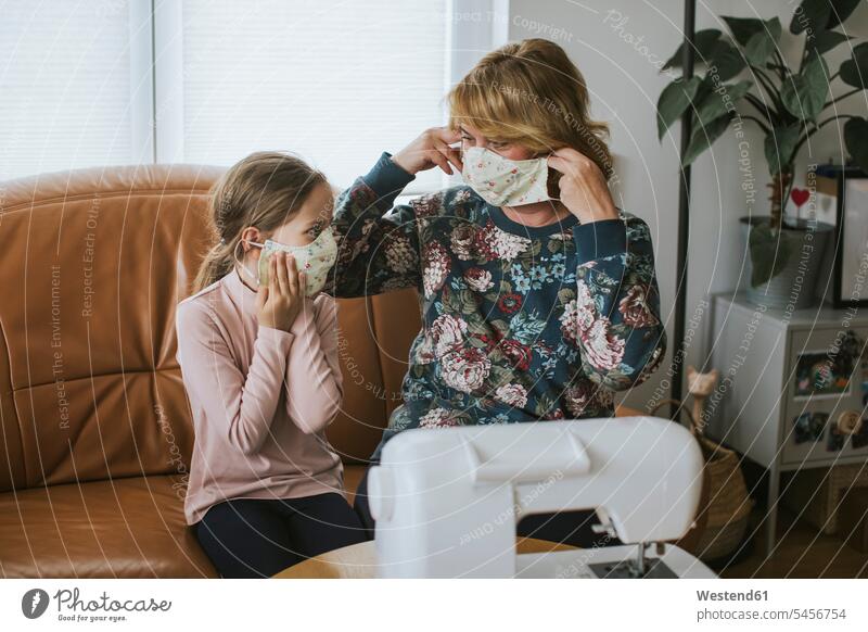Großmutter und Enkelin tragen Schutzmasken, während sie zu Hause auf dem Sofa im Wohnzimmer sitzen Farbaufnahme Farbe Farbfoto Farbphoto Deutschland
