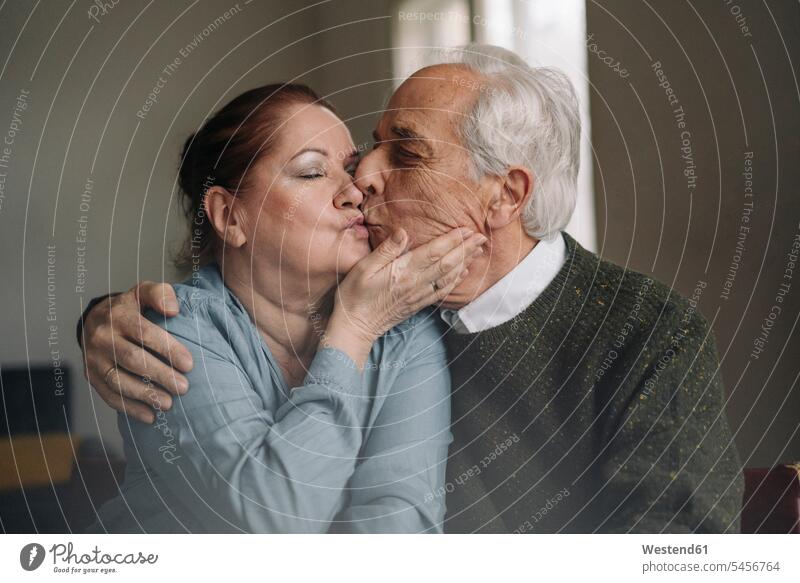 Älteres Paar küsst sich zu Hause sitzend sitzt Arm umlegen Umarmung Umarmungen entspannen relaxen entspanntheit relaxt freuen geniessen Genuss Glück
