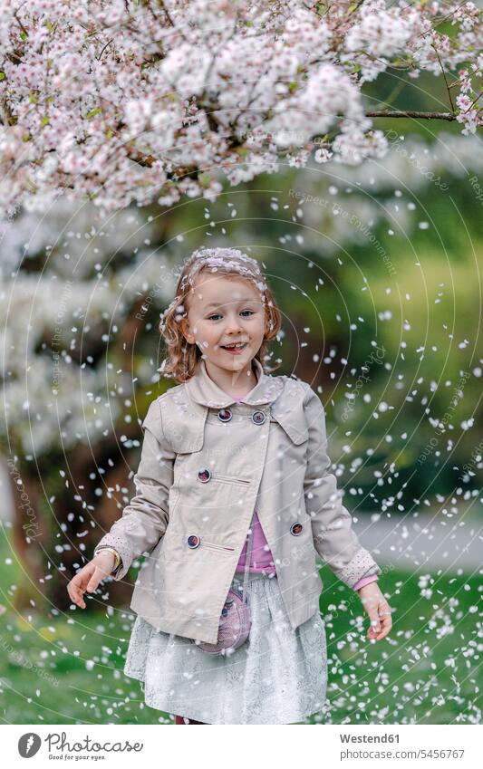 Porträt eines glücklichen kleinen Mädchens in einem Park, das unter einem blühenden japanischen Kirschbaum steht Leute Menschen People Person Personen