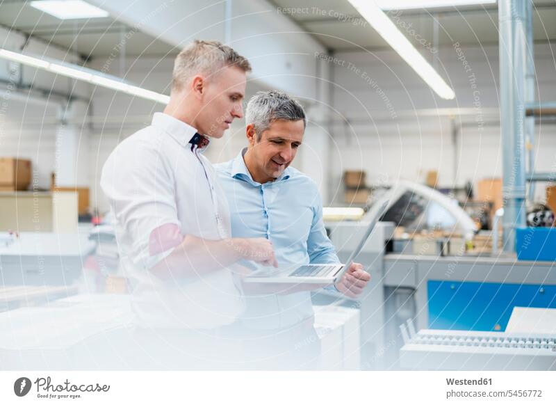 Zwei Kollegen diskutieren mit Laptop in einer Fabrik Arbeitskollege Arbeitskollegen Job Berufe Berufstätigkeit Beschäftigung Jobs geschäftlich Geschäftsleben