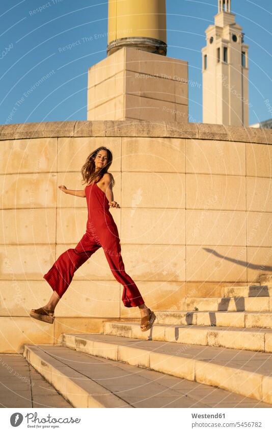 Spanien, Barcelona, Montjuic, junge Frau in rotem Jumpsuit springt auf Treppe springen hüpfen roter rotes Treppenaufgang weiblich Frauen Gebäude Sprung Spruenge