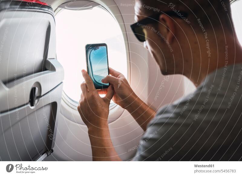 Mann im Flugzeug, mit Smartphone, ein Foto machen, Flugzeugfenster iPhone Smartphones Reisende Reisender fotografieren benutzen benützen Männer männlich Fenster