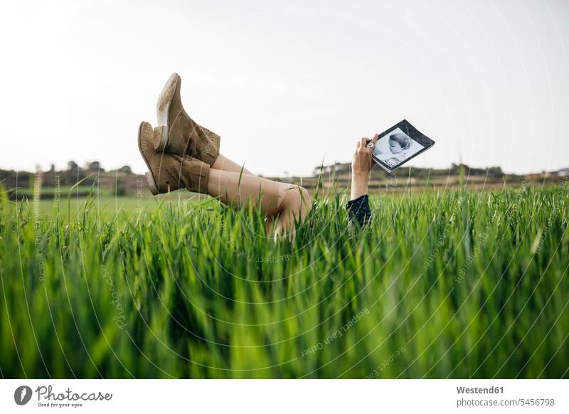 Frau liegt auf einem Feld mit Beinen in der Luft und liest ein Buch Bücher weiblich Frauen lesen Lektüre liegen liegend Felder Erwachsener erwachsen Mensch