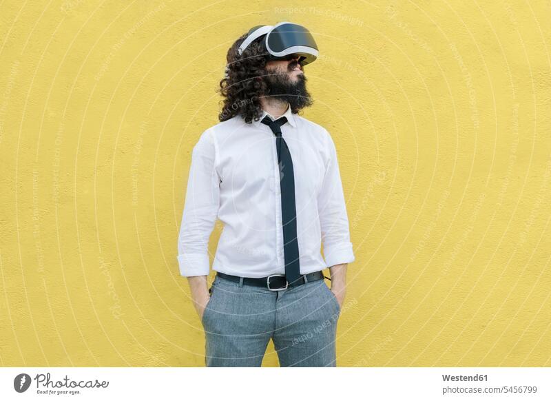 Unternehmen, das eine Virtual-Reality-Brille trägt und mit den Händen in den Taschen gegen die gelbe Wand steht Farbaufnahme Farbe Farbfoto Farbphoto