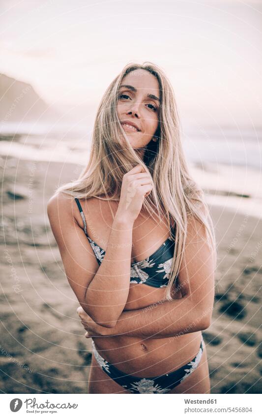 Junge blonde Frau im Bikini am Strand, die in die Kamera schaut Badebekleidung Bikinis früh Frühe Morgen freuen Glück glücklich sein glücklichsein zufrieden
