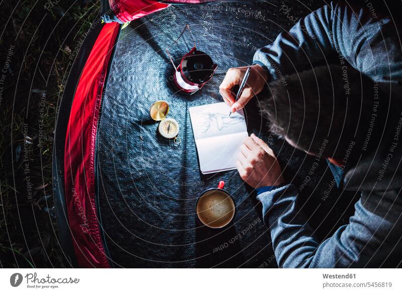 Mann zeltet in Estland und zeichnet nachts in sein Skizzenbuch Natur Kompass Magnetkompasse Kompasse Laterne Laternen Zelt Zelte Notizbuch Notizbücher