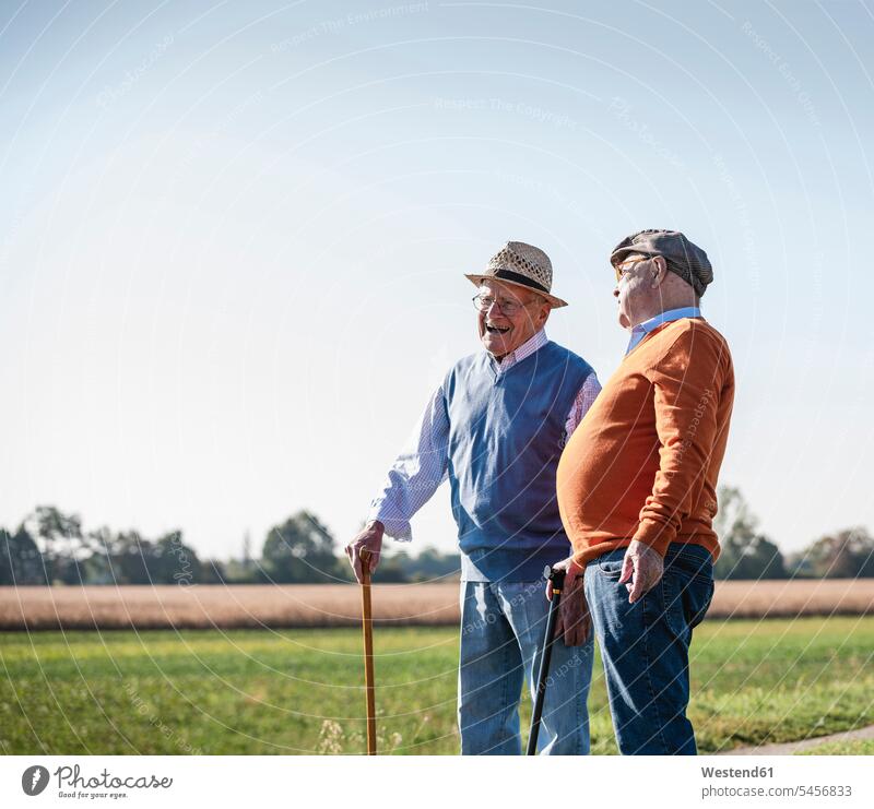 Zwei alte Freunde stehen auf den Feldern und reden über alte Zeiten gehen gehend geht Spaziergang Beste Freunde Bester Freund lachen betrachten betrachtend