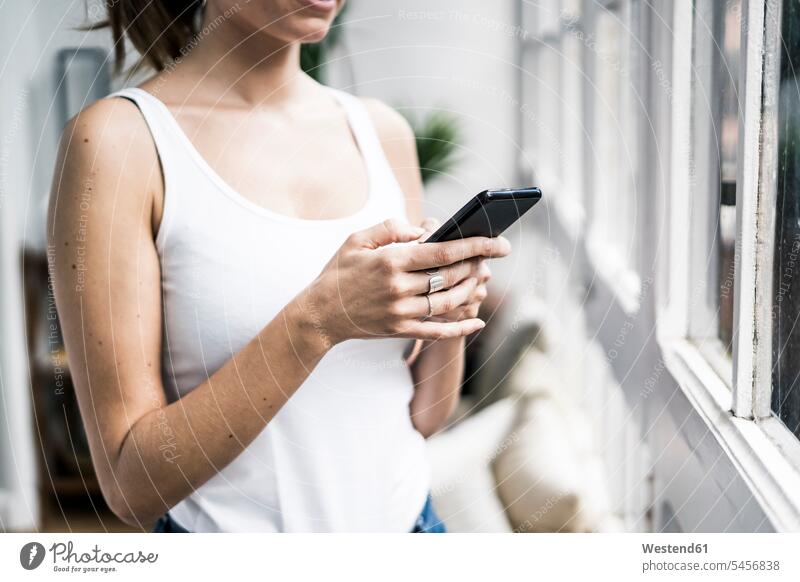 Nahaufnahme einer Frau, die ein Mobiltelefon am Fenster zu Hause benutzt Handy Handies Handys Mobiltelefone weiblich Frauen Zuhause daheim Telefon telefonieren