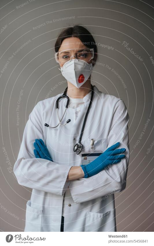 Ärztin mit Maske und Schutzbrille mit verschränkten Armen an der Wand stehend im Krankenhaus Farbaufnahme Farbe Farbfoto Farbphoto Innenaufnahme Innenaufnahmen
