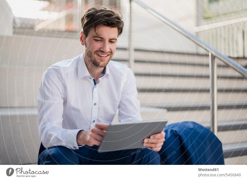 Lächelnde Geschäftsmann sitzt auf der Treppe in der Stadt mit Tablette sitzen sitzend Tablet Computer Tablet-PC Tablet PC iPad Tablet-Computer lächeln