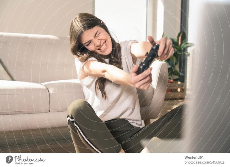 Glückliche junge Frau spielt Videospiel zu Hause Deutschland Videospiele Spielkonsole Spielkonsolen Konsole Computerspiel Computerspiele Wohnung wohnen
