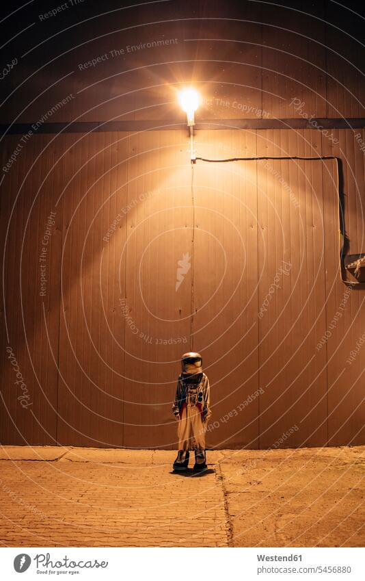 Raumfahrer stehend unter Lampe an einer Wand bei Nacht Astronaut Astronauten Weltraumfahrer nachts Wände Waende steht Leuchte Lampen Raumfahrt Beleuchtung