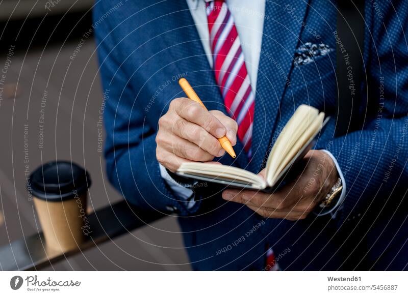 Nahaufnahme eines Geschäftsmannes, der im Freien in sein Tagebuch schreibt schreiben aufschreiben notieren schreibend Schrift Businessmann Businessmänner