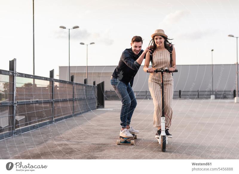 Junger Mann und Frau fahren auf Longboard und Elektroroller auf dem Parkdeck Leute Menschen People Person Personen Europäisch Kaukasier kaukasisch 2 2 Menschen