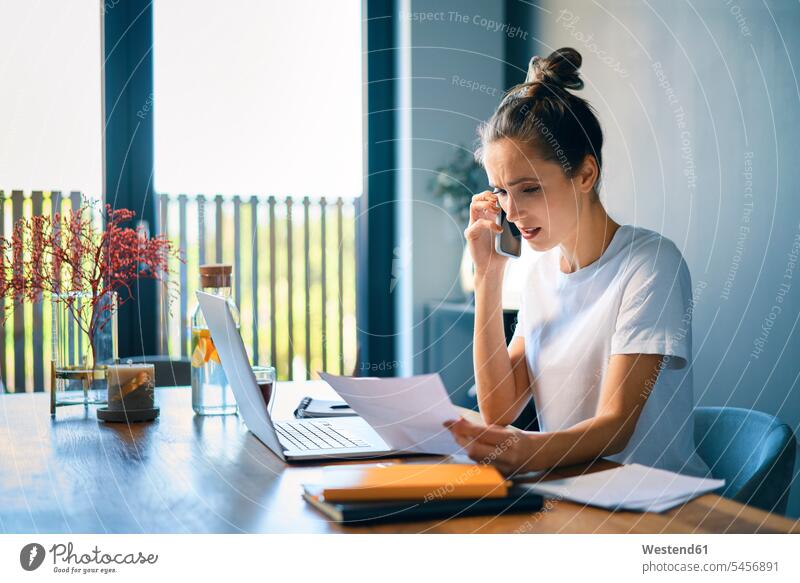 Geschäftsfrau hält Dokument in der Hand und spricht über Smartphone am Schreibtisch im Home-Office Farbaufnahme Farbe Farbfoto Farbphoto Freizeitkleidung