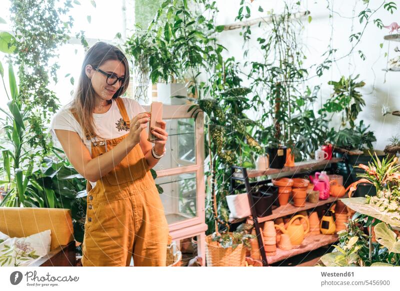 Junge Frau beim Fotografieren mit einem Smartphone in einem kleinen Gartengeschäft Job Berufe Berufstätigkeit Beschäftigung Jobs Bilder Bildnis Fotos
