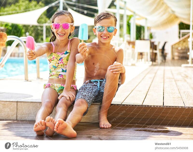 Porträt eines fröhlichen kleinen Mädchens und Jungen mit verspiegelter Sonnenbrille, die ihre Eis am Stiel zeigen Leute Menschen People Person Personen